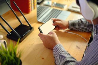 Środkowa sekcja mężczyzny używającego smartfonu siedząc przy biurku w biurze