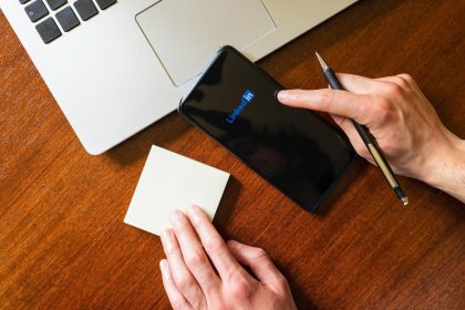 Dłoń dotykająca smartfona z aplikacją linkedin na biurku