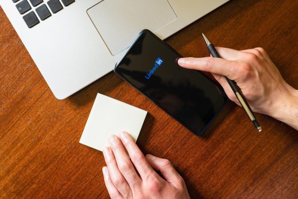 Dłoń dotykająca smartfona z aplikacją linkedin na biurku