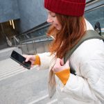 Uśmiechnięta dziewczyna chodząca po schodach za pomocą wiadomości tekstowej z telefonu komórkowego po drodze za pomocą aplikacji na smartfona ma