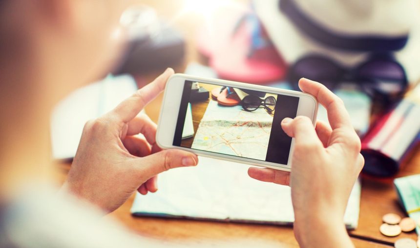 koncepcja wakacji, turystyki, podróży, technologii i ludzi - zbliżenie kobiety ze smartfonem fotografującej mapę i rzeczy podróżne