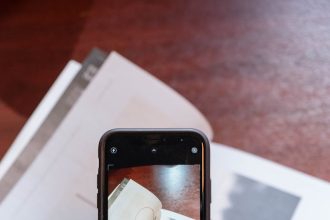 Person photographing a book with a smartphone indoors on a wooden table.