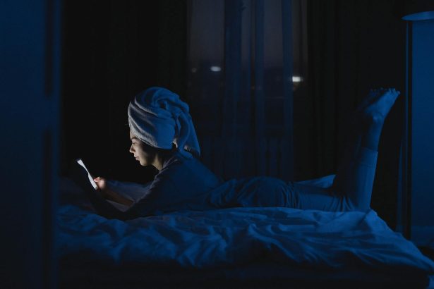 A woman lying in bed with a towel on her head, using a mobile phone at night.