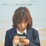 Girl in uniform looks at her phone by the sea.