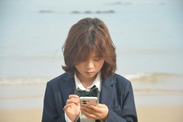 Girl in uniform looks at her phone by the sea.