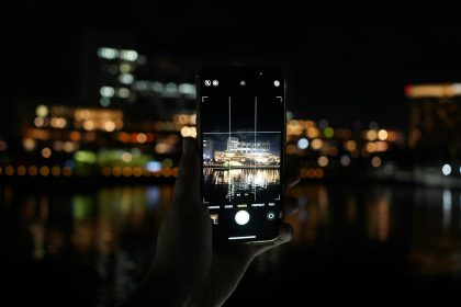 Hand holding phone capturing city lights at night.