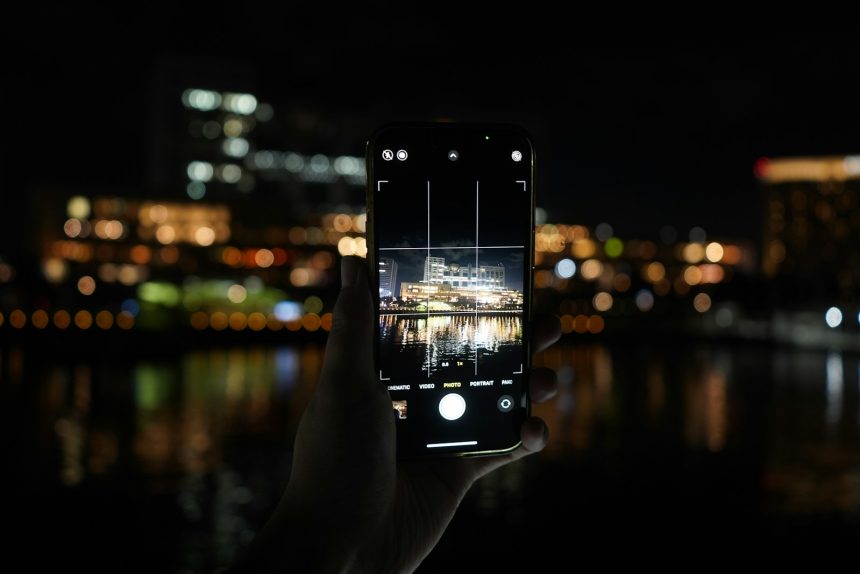 Hand holding phone capturing city lights at night.