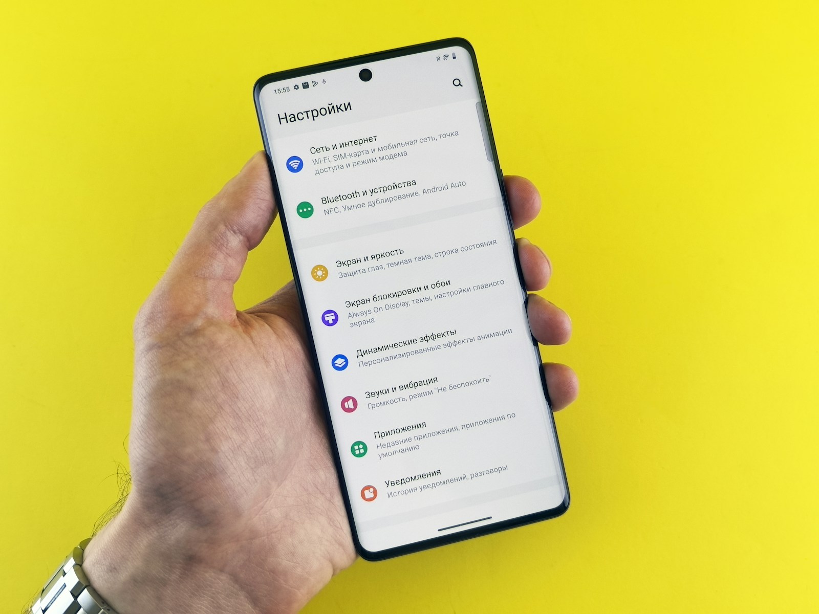 A hand holds a phone with settings displayed.